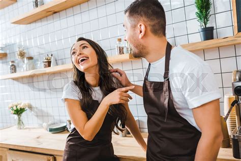 Cashiers In Aprons Talking And Laughing Near Bar Counter In Coffee