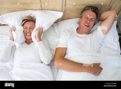 Annoyed Woman Covering Ears With Pillow While Man Snoring On Bed In