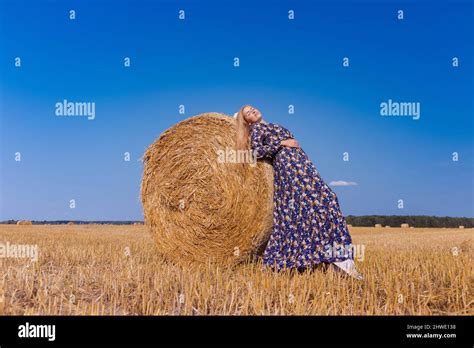 Une jeune fille blonde aux cheveux longs dans un chapeau blanc se repose et pose près des gerbes