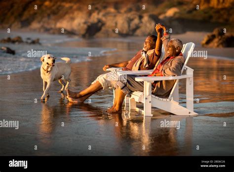 Mature Couple Relaxing In Deck Chairs On A Beach At Sunset Stock Photo Alamy