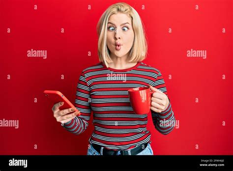 Jeune femme blonde utilisant un smartphone et buvant une tasse de café faisant le visage de