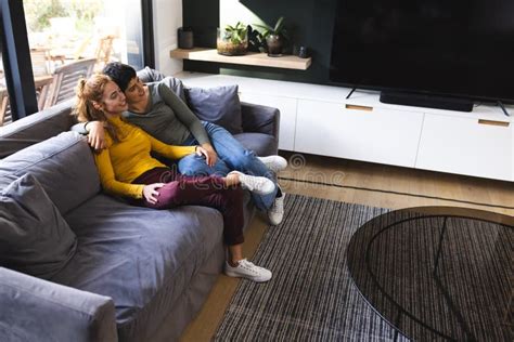 Portrait Of Happy Biracial Lesbian Couple Embracing And Smiling On Couch At Home Stock Image