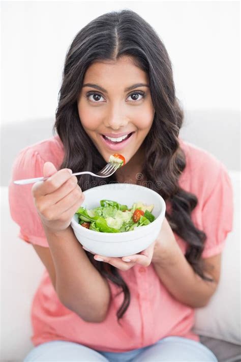Smiling Cute Brunette Sitting On Couch Holding Salad Bowl Stock Photo