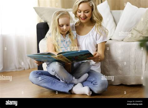 Bonne famille Une jeune mère blonde lit un livre à sa jolie fille tout en étant assise au sol