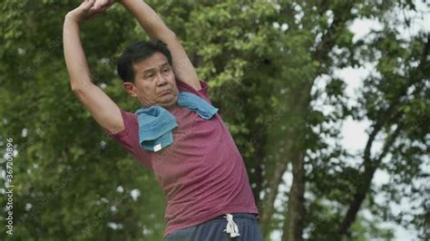 Asian Mature Man Doing Arm Stretching Warm Up Before Exercise In The Outdoor Park With Trees