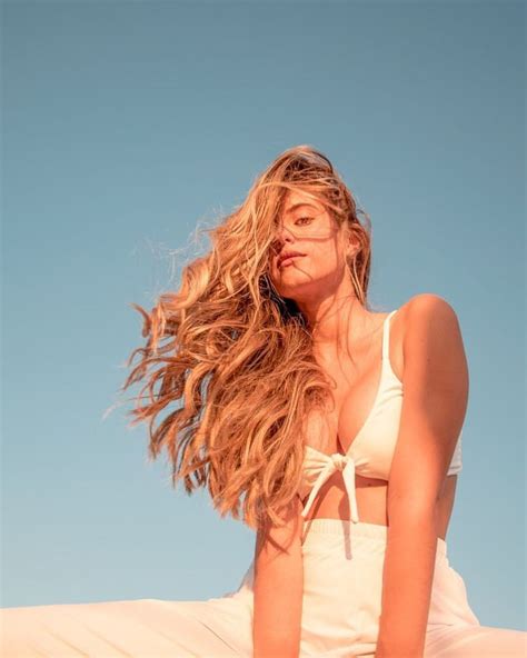 A Woman Sitting On Top Of A Sand Dune With Her Hair Blowing In The Wind