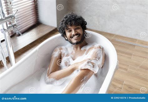 Happy Naked Indian Man Taking Bath At Home Laying In White Bathtub With Foam And Smiling At