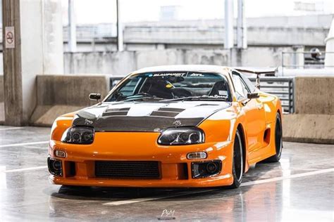 an orange and black car parked in a parking lot next to some concrete pillars with windows