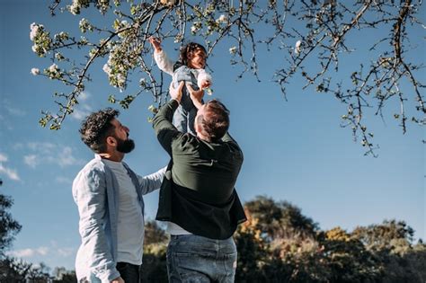 Casal gay masculino levantando sua filha para tocar as flores de uma árvore conceito de família