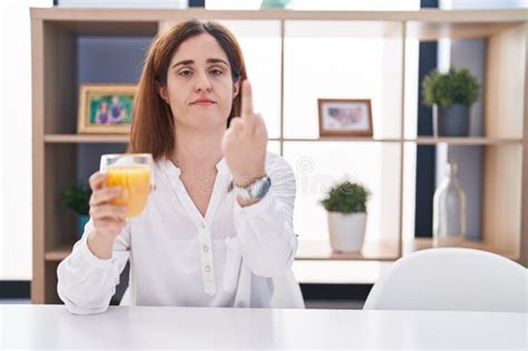 Brunette Woman Drinking Glass Of Orange Juice Showing Middle Finger Impolite And Rude Off