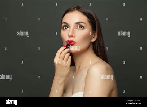 Young Woman Applying Red Lipstick Makeup On Lips On Black Background