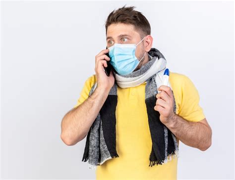Anxieux jeune homme malade blonde portant un masque médical et un foulard parle au téléphone et