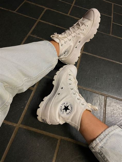 A Person Wearing White Sneakers And Jeans Standing On A Tile Floor