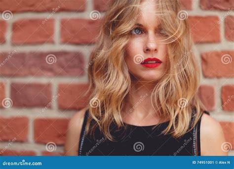 Caucasian Blond Woman Standing Behind Brick Wall And Looking Away Stock