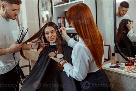 Professional makeup artist and hairstylist preparing female customer in