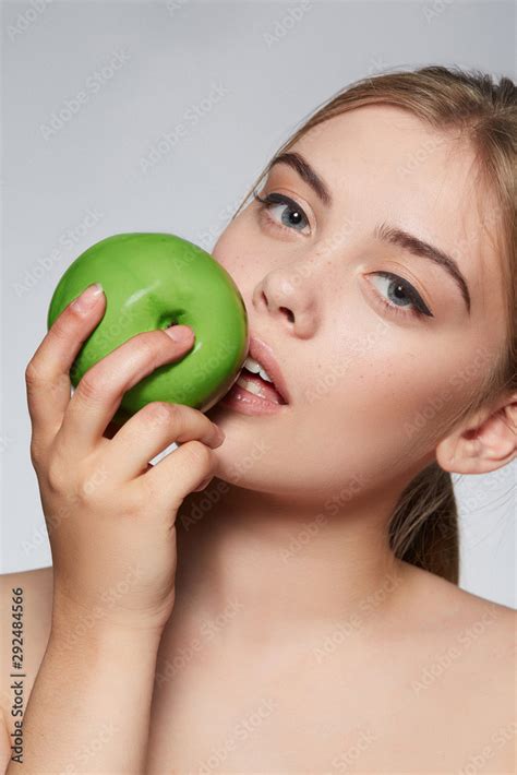 Close Up Portrait Of A Blond Girl With Naked Shoulders She Bites A Green Apple Girl Has Nude