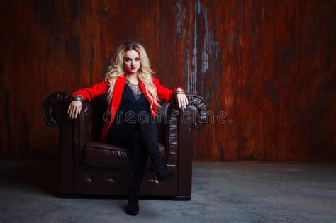 Junge Und Attraktive Blonde Frau In Der Roten Jacke Sitzt Im Ledersessel Rostige Wand Des