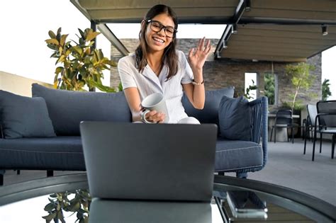 Alegre joven latina saludando en una videollamada desde su computadora portátil en el interior