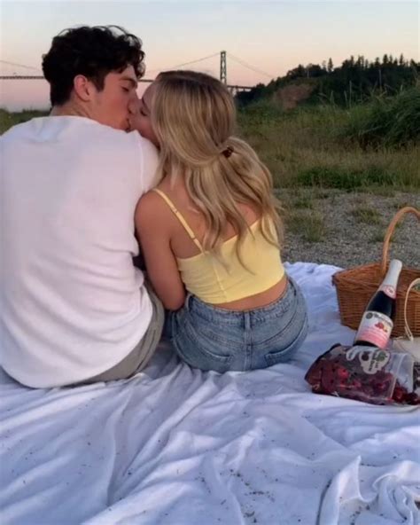 A Man And Woman Sitting On A Blanket Kissing