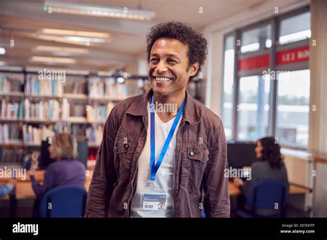 Portrait Of Mature Male Teacher Or Student In Library With Other Students Studying In Background