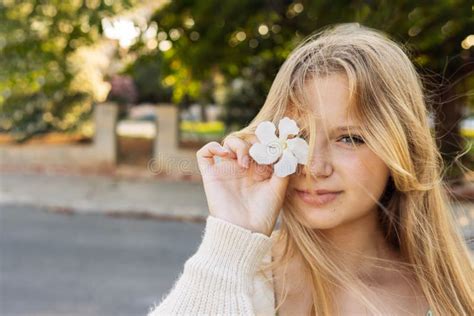 Portrait Of A Teenage Girl Of European Blonde Hair Stands On The Street Holding A White Flower