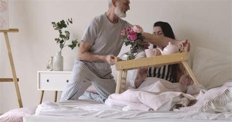 Brunette Caucasian Woman Lying As Handsome Husband Bringing Bed Tray With Tea Croissants And