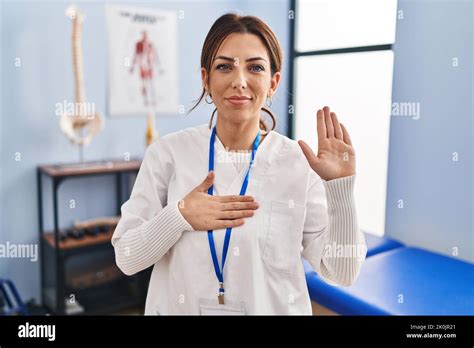 Jeune femme brunette travaillant à la clinique de récupération de la douleur jurant avec la main