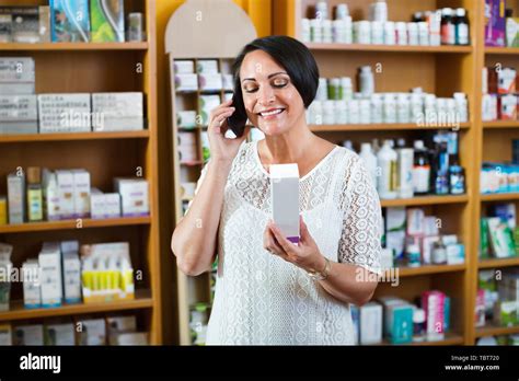 Happy Charming Smiling Mature Brunette Woman Chatting By Phone While Shopping In Drugstore Stock