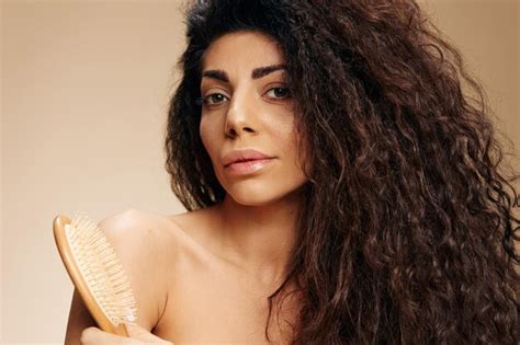 Sonriente dama latina bastante rizada sostiene el cepillo para el cabello después de la rutina