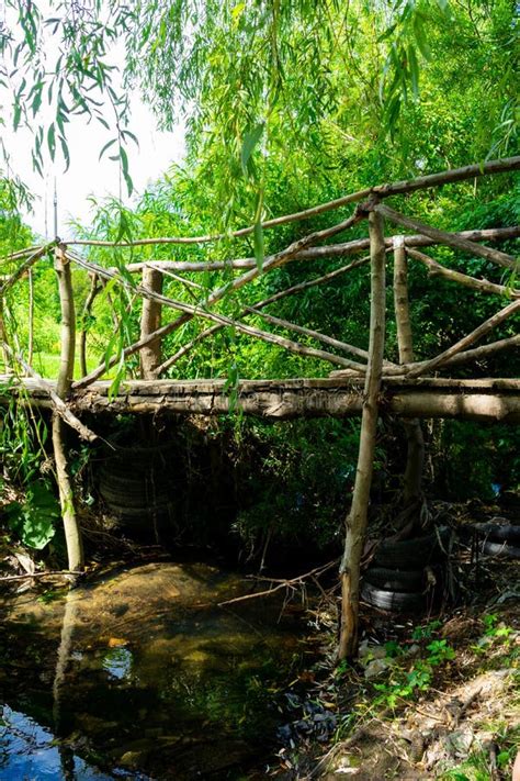 A Wooden Bridge Over A Small River Under The Canopy Of Green Trees