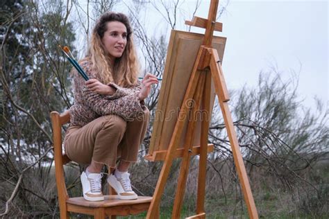 Jeune Femme Blonde Peignant Dans Un Champ Avec Des Pinceaux Et Un Chevalet Photo Stock Image