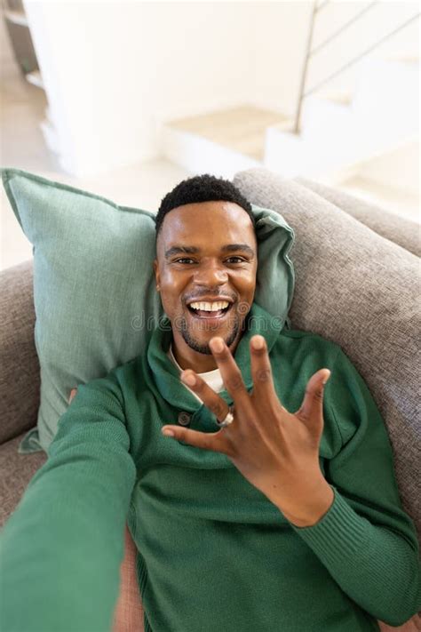 Portrait Of Happy African American Gay Man Showing Wedding Ring While Lying On Sofa In Living