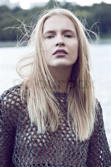Portrait Of Beautiful Blonde Woman In Transparent Jacket And Black Skirt Poses Near Water