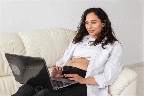 mujer embarazada latina usando una computadora portátil sentada en un sofá en casa embarazo e