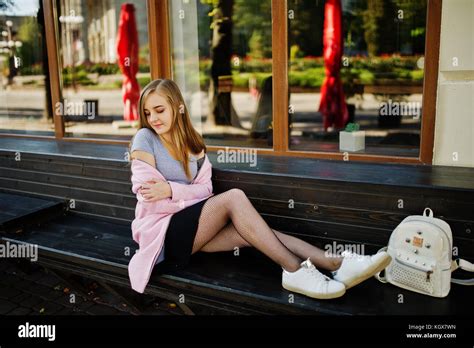 Jeune fille blonde en jupe noire et manteau rose avec sac à dos femme assis sur le banc à la