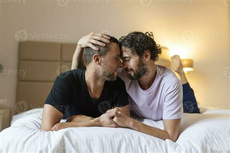 Happy Gay Couple Lying Down On The Bed At Home Hugging And Flirting LGBT Gay Couple Love