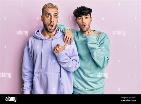 Homosexual Gay Couple Standing Together Wearing Casual Clothes Surprised Pointing With Hand