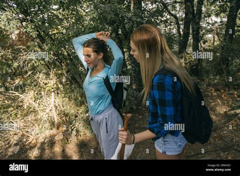 Beautiful Brunette Hiker Girl Fixing Her Hair At The Forest While Standing With Her Friend Stock