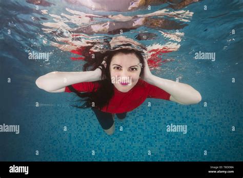 Portrait Of A Smiling Long Haired Brunette Woman In A Red T Shirt Underwater In A Swimming Pool
