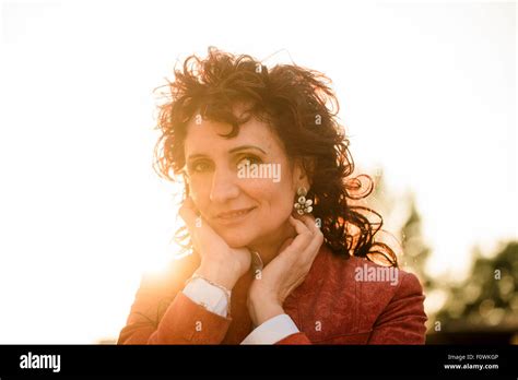 Portrait Of Smiling Mature Woman In Red Jacket Enjoying Life With Sun In Background Stock Photo
