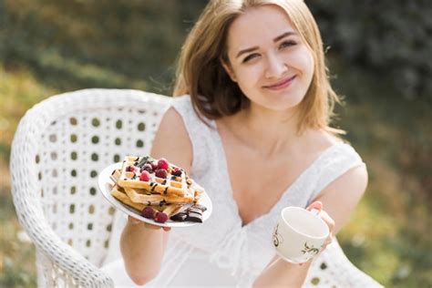 Lächelnde blonde junge Frau Platte von Waffeln und von Kaffeetasse zeigt Kostenlose Foto