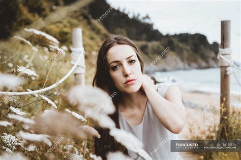 Tender Brunette Woman By Flowers On Coast Natural Emotionless Stock Photo