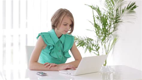 Blonde Girl Sitting At Office Desk Using Laptop Holding Apple Looking At Camera And Smiling
