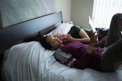 High Angle View Of Lesbian Couple Lying On Bed While Using Digital