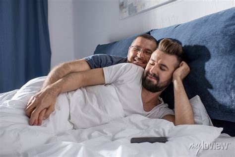Feliz casal gay deitado na cama e de mãos dadas cartazes para a parede posters