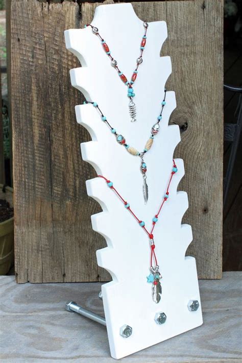 A White Wooden Stand With Beads And Necklaces On It S Sides Next To A