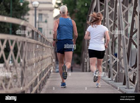 Healthy Mature Couple Jogging In The City At Early Morning With Sunrise In Background Stock