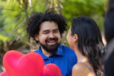 Joven pareja latina mexicana riendo y hablando en el día de san valentín con globos rojos en