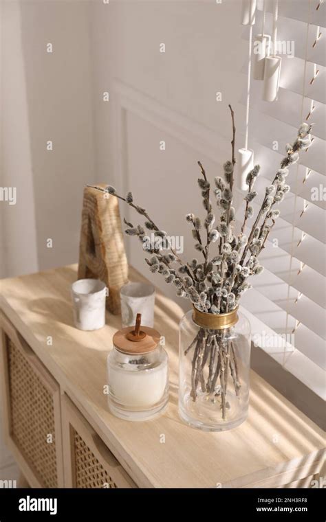 Glass Vase With Pussy Willow Tree Branches And Candle On Wooden Commode Near Window In Room