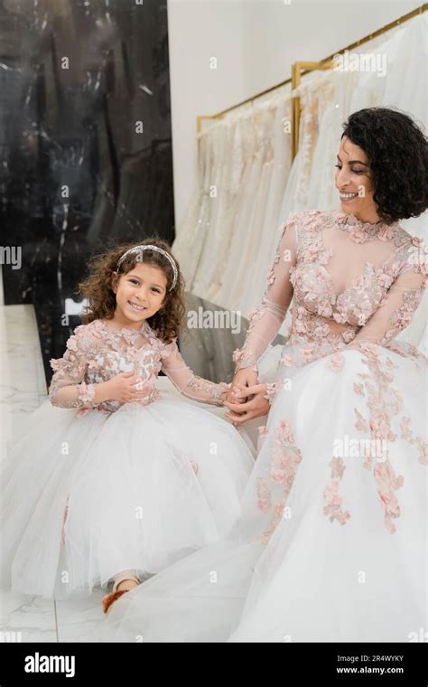 Brunette Middle Eastern Woman With Wavy Hair Looking At Cheerful Girl And Smiling Near White